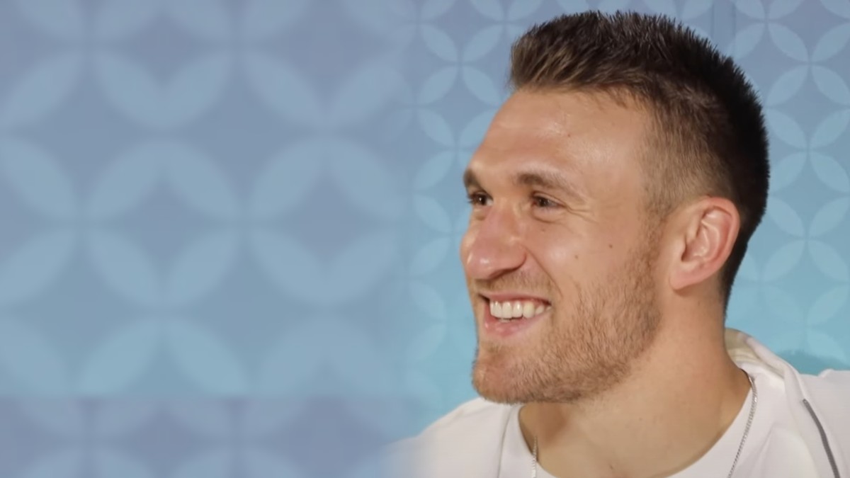 Kyle Juszczyk smiling at a podium during Super Bowl media week
