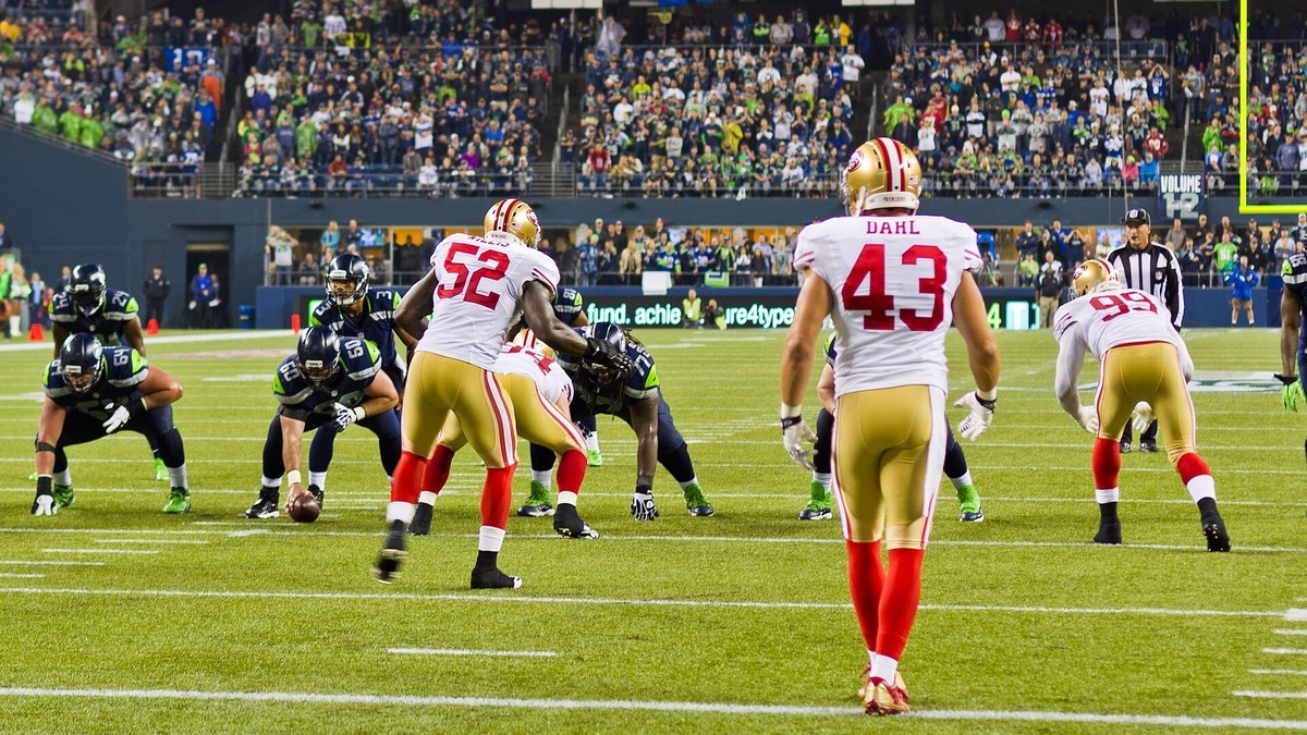49ers defenders in white road uniforms lined up against the Seahawks offense at Lumen Field in Seattle