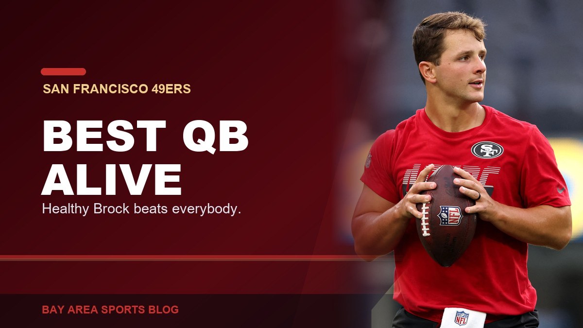 Brock Purdy in a red 49ers warmup shirt holding a football before a preseason game