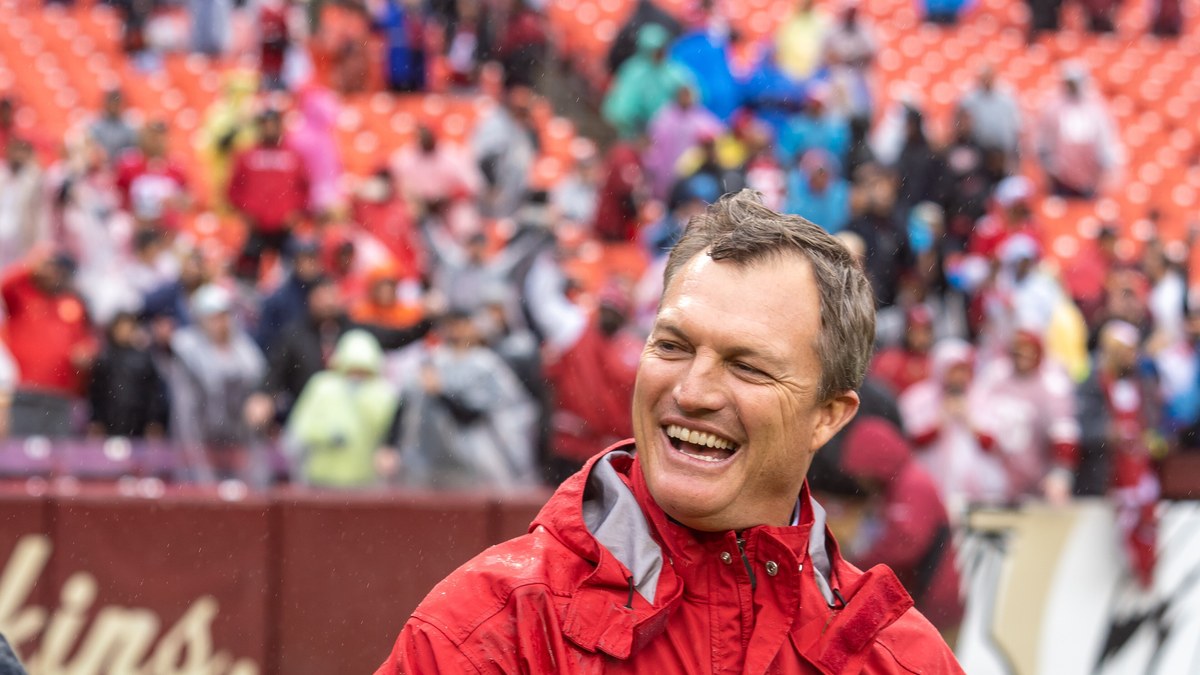 John Lynch laughing on the field in a red 49ers rain jacket after a game