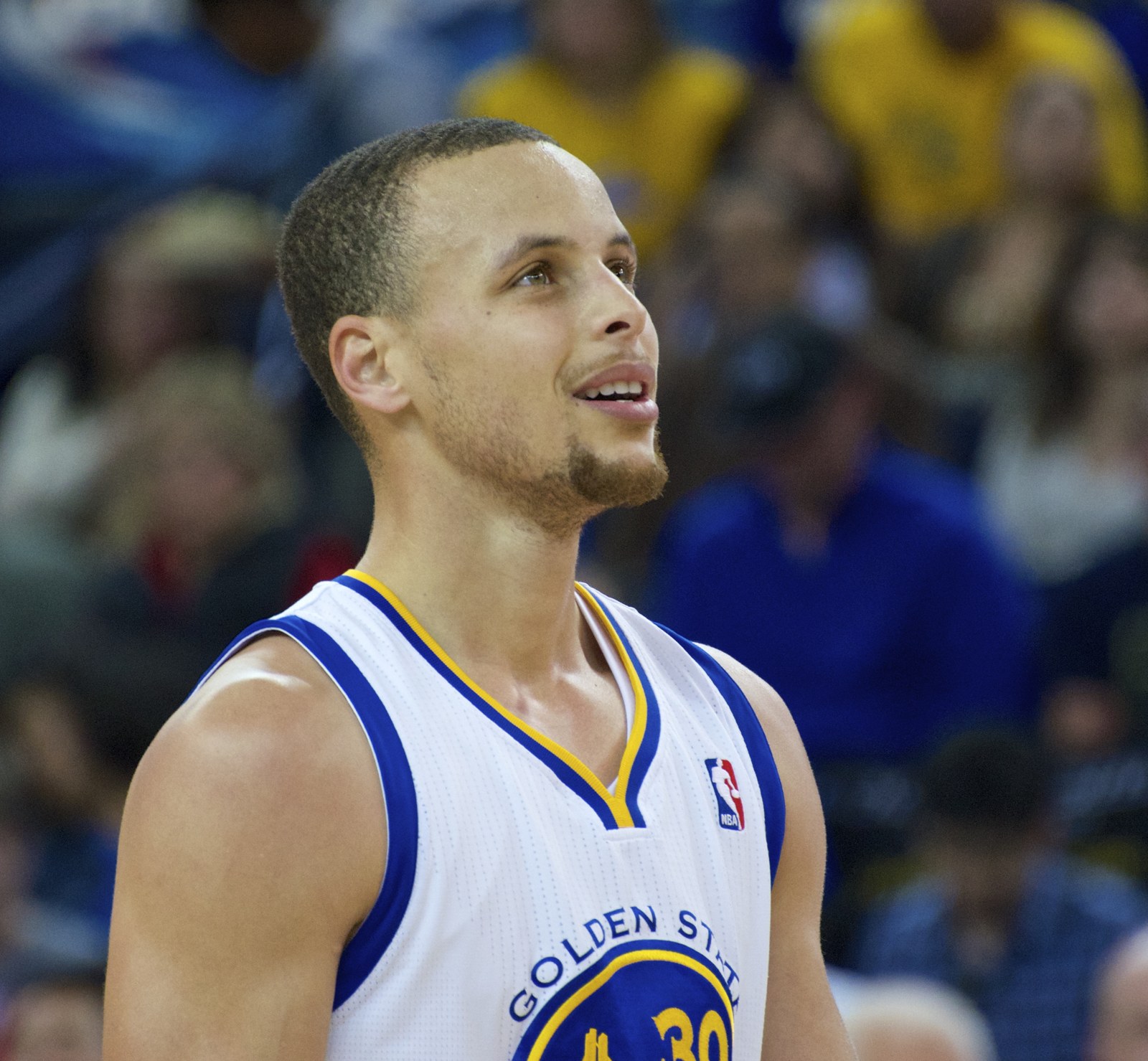 Stephen Curry in his white Golden State Warriors home jersey, number 30, looking up and smiling at Oracle Arena