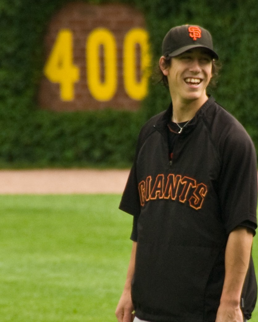 Tim Lincecum laughing on the field in a black San Francisco Giants warmup jacket and cap