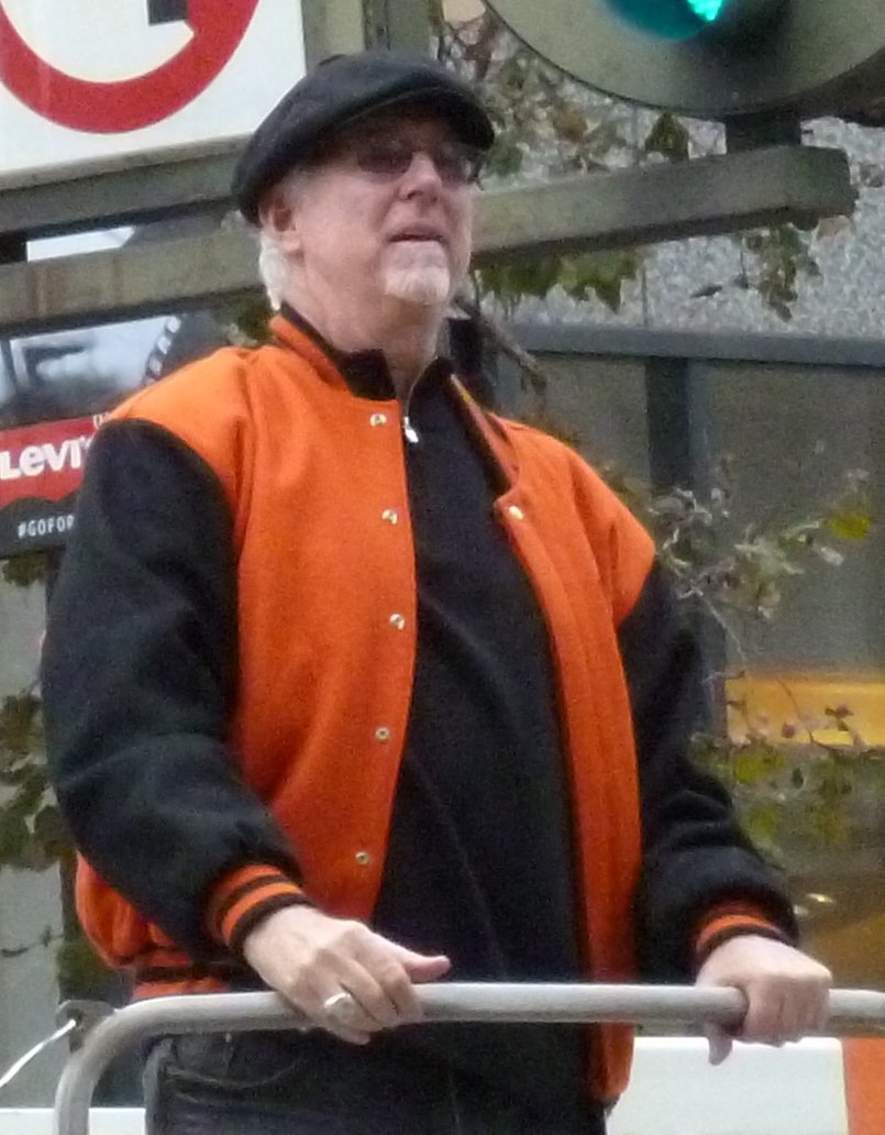 Mike Krukow in an orange and black Giants jacket riding in the 2012 World Series victory parade in San Francisco