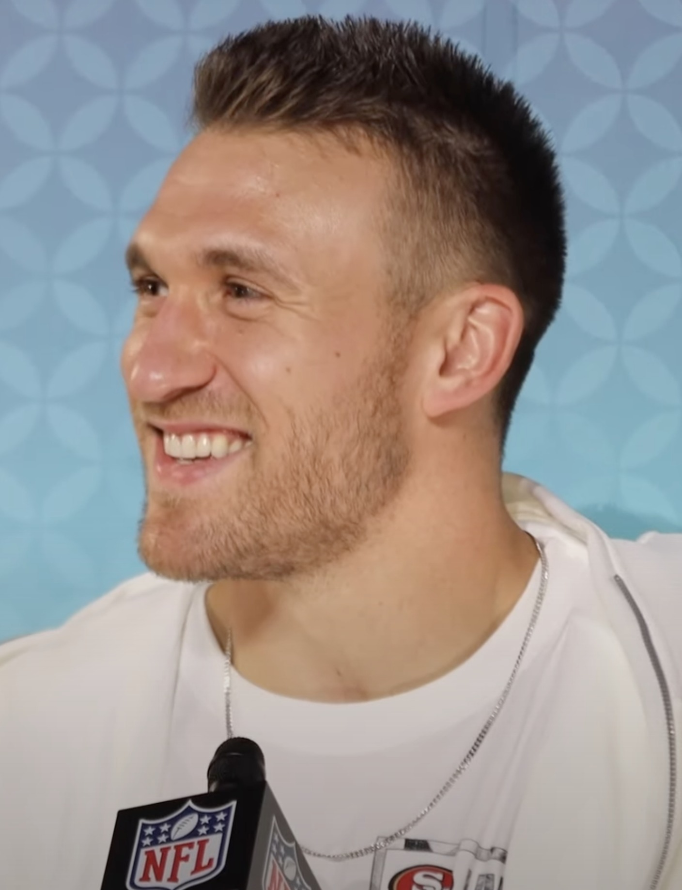 Kyle Juszczyk smiling at a podium during Super Bowl media week