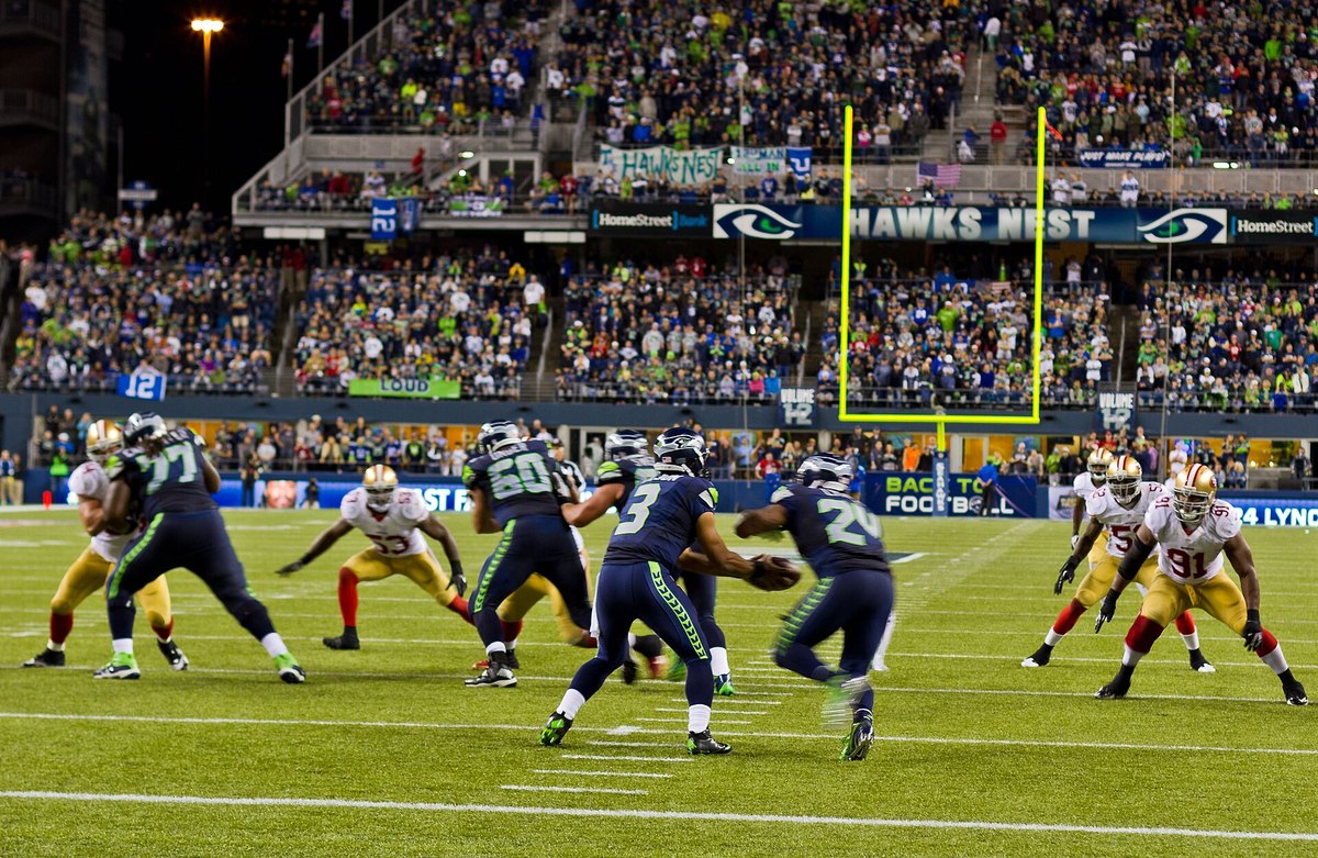 Seahawks quarterback handing off as 49ers defenders close in during a night game in Seattle